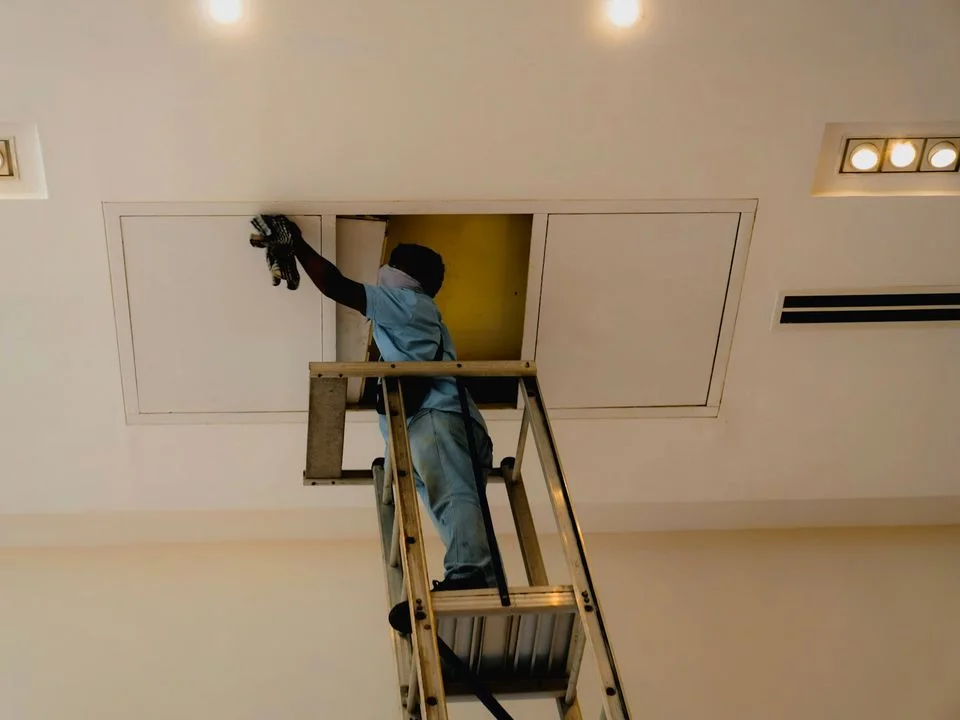 Eletricista sobre escada passando fiação e preparando pontos de luz durante a obra